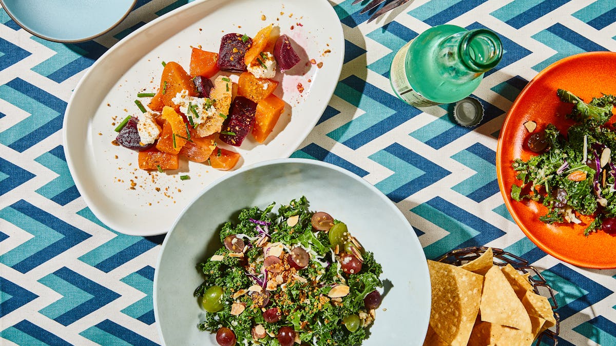 A plate of salad, a plate of vegetables, and a bottle of soda on a table