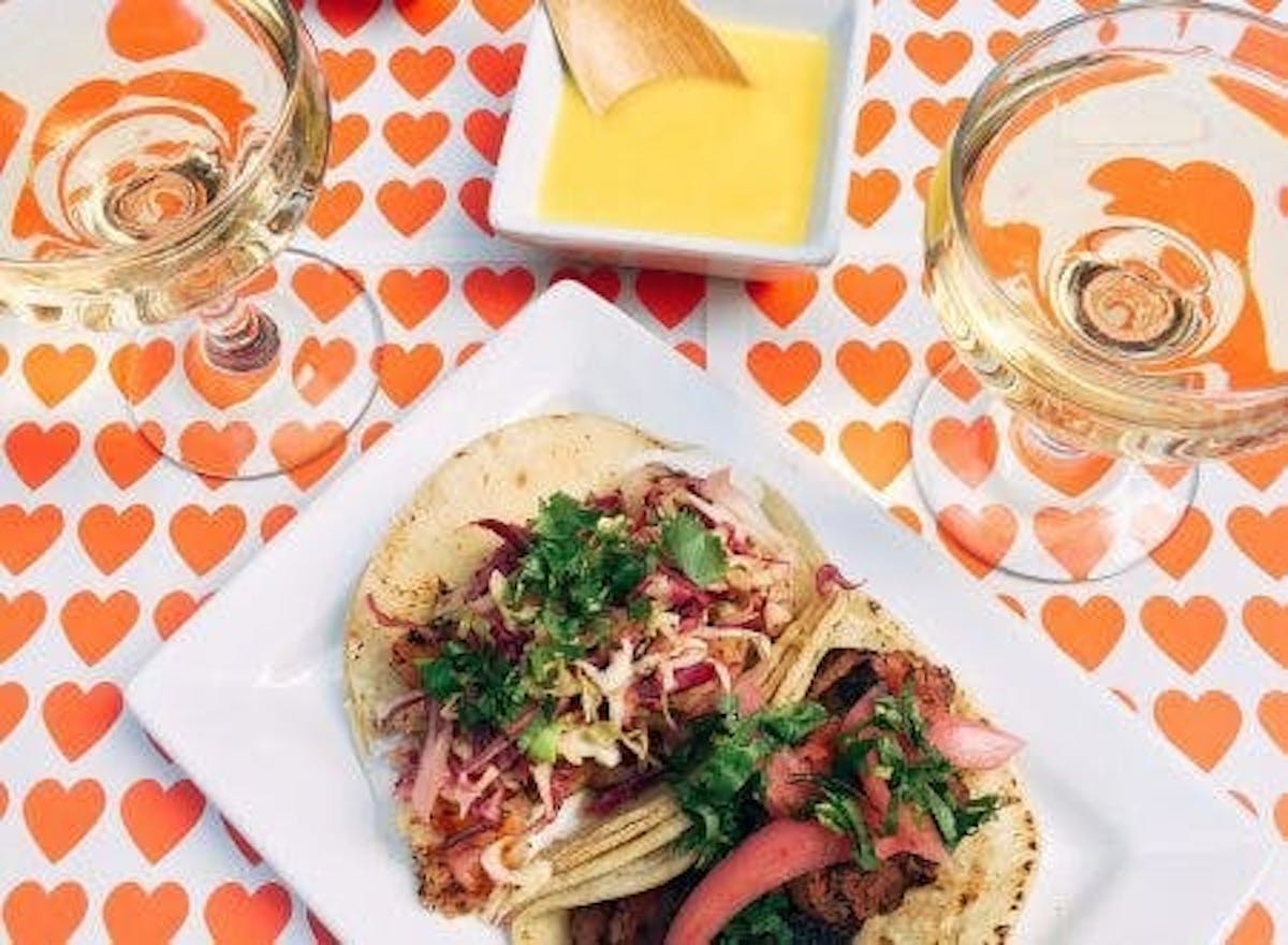 a photo of a heart pattern table with camera zooming over the food and two glasses of wine with a plate of two tacos and a sauce