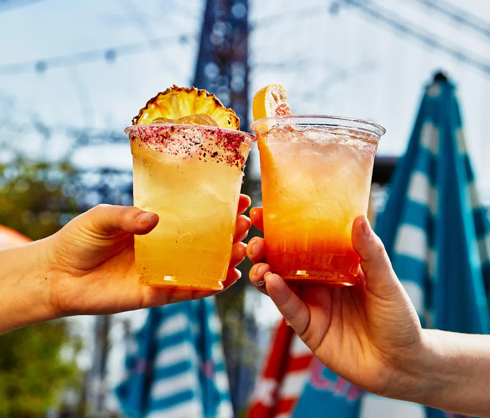 two hands holding drinks with a tower in the background