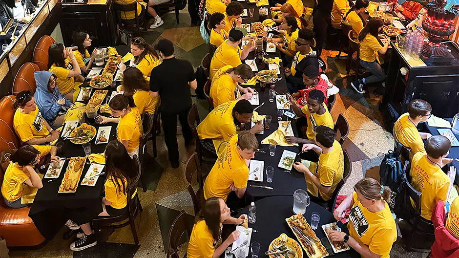 Students in yellow shirts eating at tables during school group dining near Central Park, Manhattan, NY.