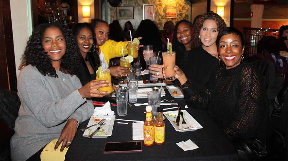 Six women sitting at a table and holding up drinks during Kips Bay, Manhattan travel & tour group dining.