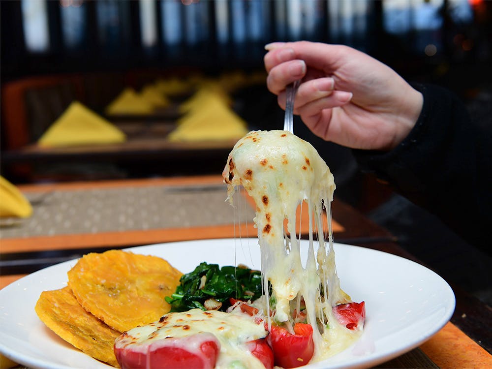 Woman's hand holding a fork over a plate of Pimientos Rellenos, one of our Bowery, Manhattan, NYC vegetarian dishes.