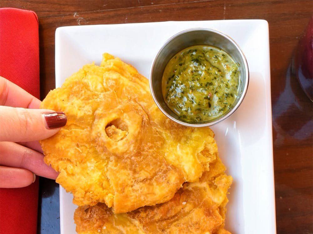 Woman's hand holding Tostones on a plate, part of our vegetarian food near Williston Park, New York.