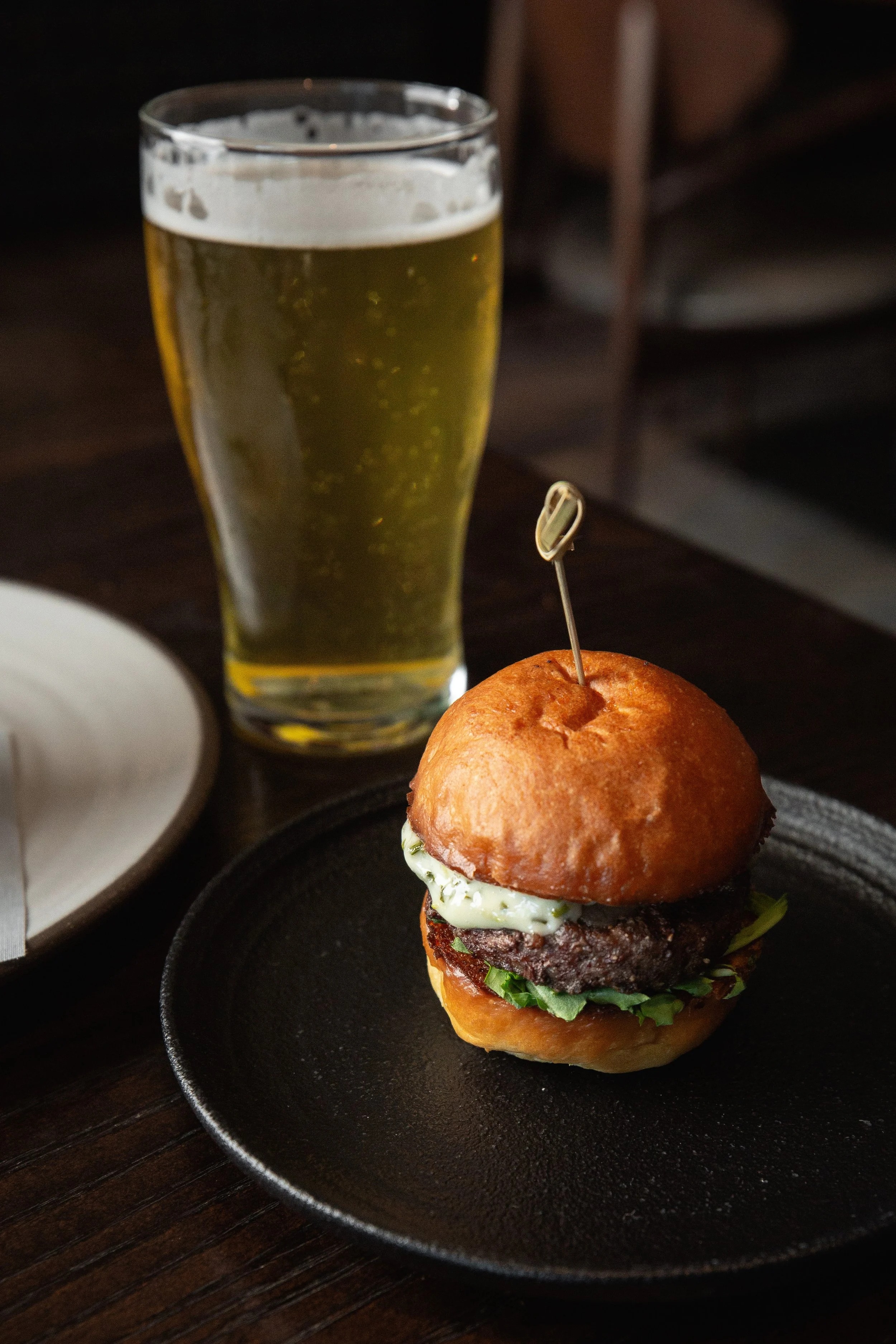 a burger on a plate next to a glass of beer