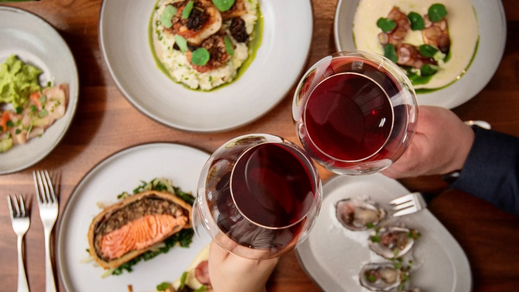 a person holding wine glasses with food on plates