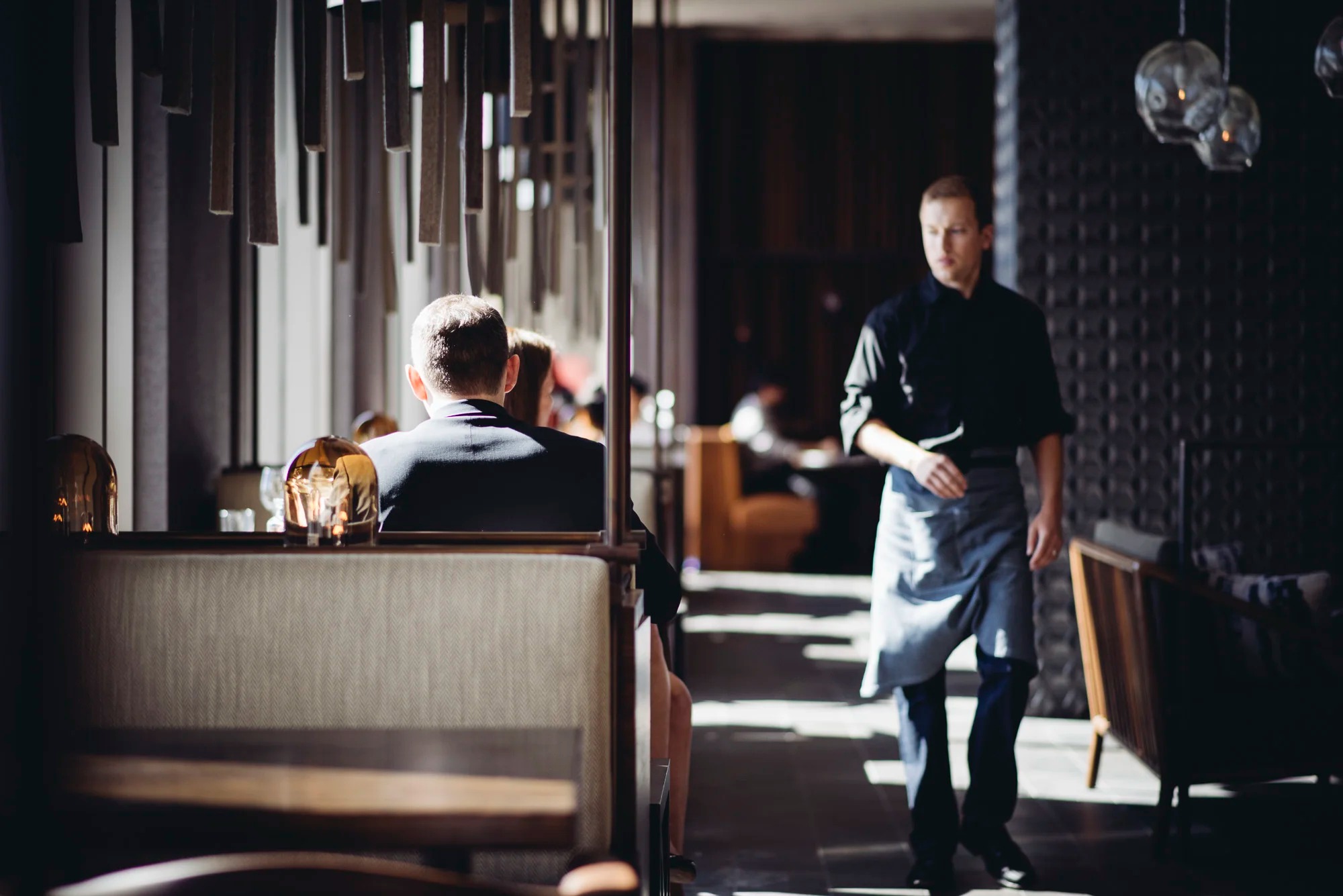 a man in a black shirt and apron walking towards a man in a black shirt