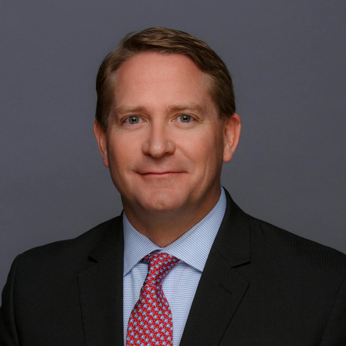 a man wearing a suit and tie smiling and looking at the camera