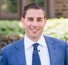 a man wearing a suit and tie smiling at the camera