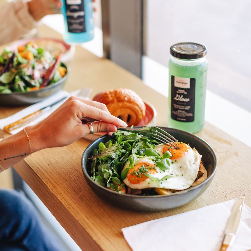 Sunny-side-up eggs with greens and toast, served alongside a croissant and cold-pressed juice — a fresh and vibrant option for the best breakfast in Del Mar.
