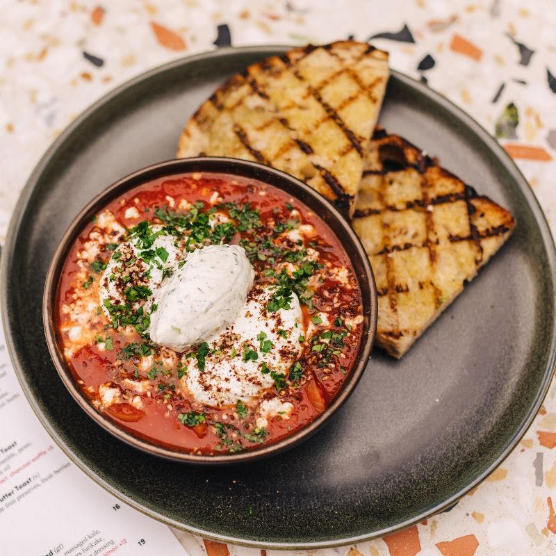 Vegetarian shakshuka with poached eggs, za’atar, labneh, and feta, served with grilled bread — a flavorful Mediterranean-style breakfast in La Jolla.