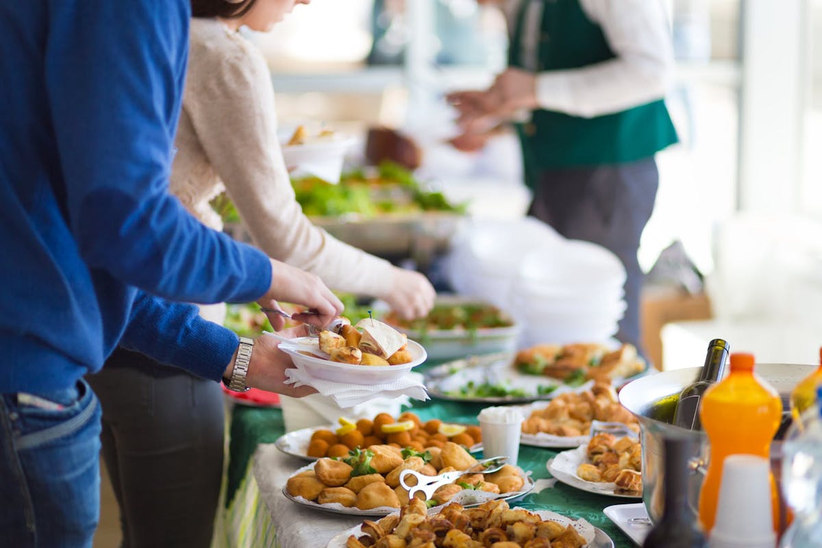 a group of people serving food from a table filled with multiple plates of food
