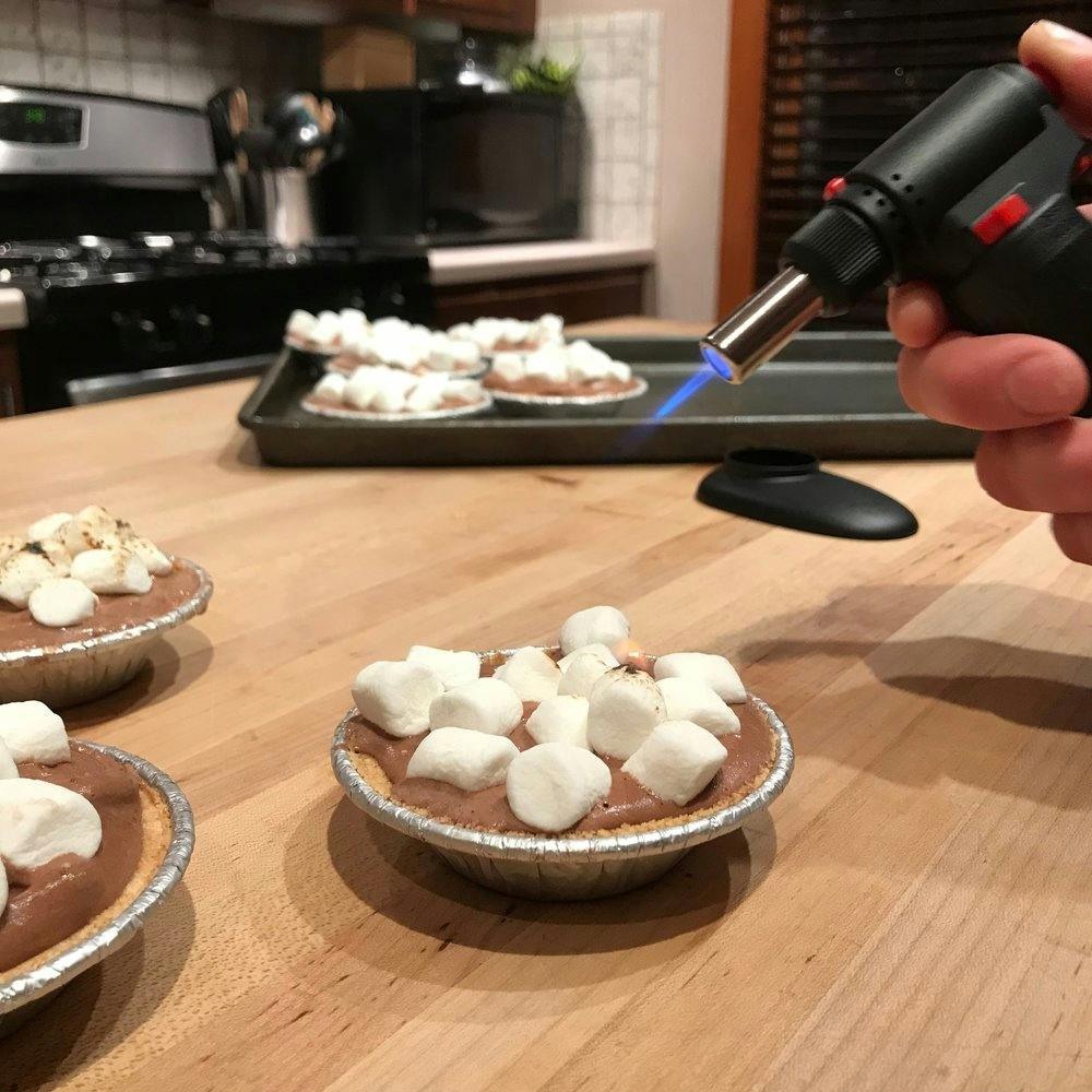 an ice cream cup topped with marshmallows being flamed with a kitchen torch