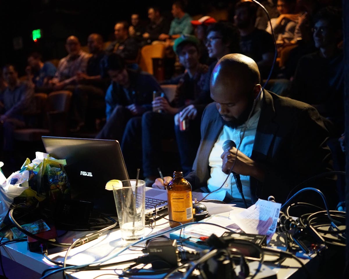 a man sitting at a table with a laptop in front of a crowd
