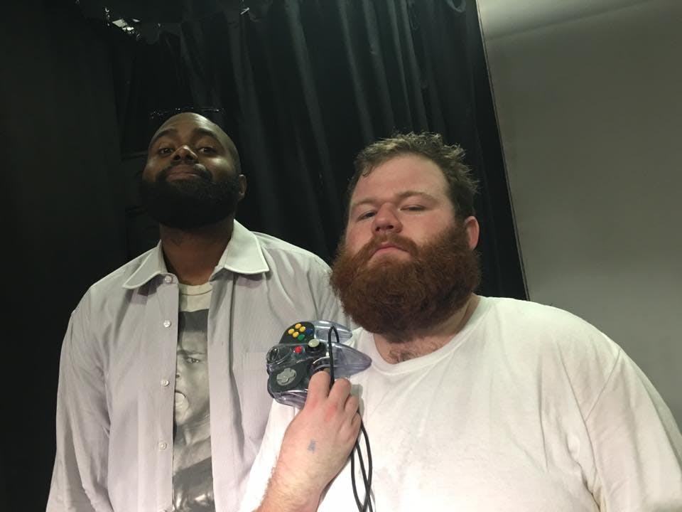 two men posing for the camera, one with a video game controller