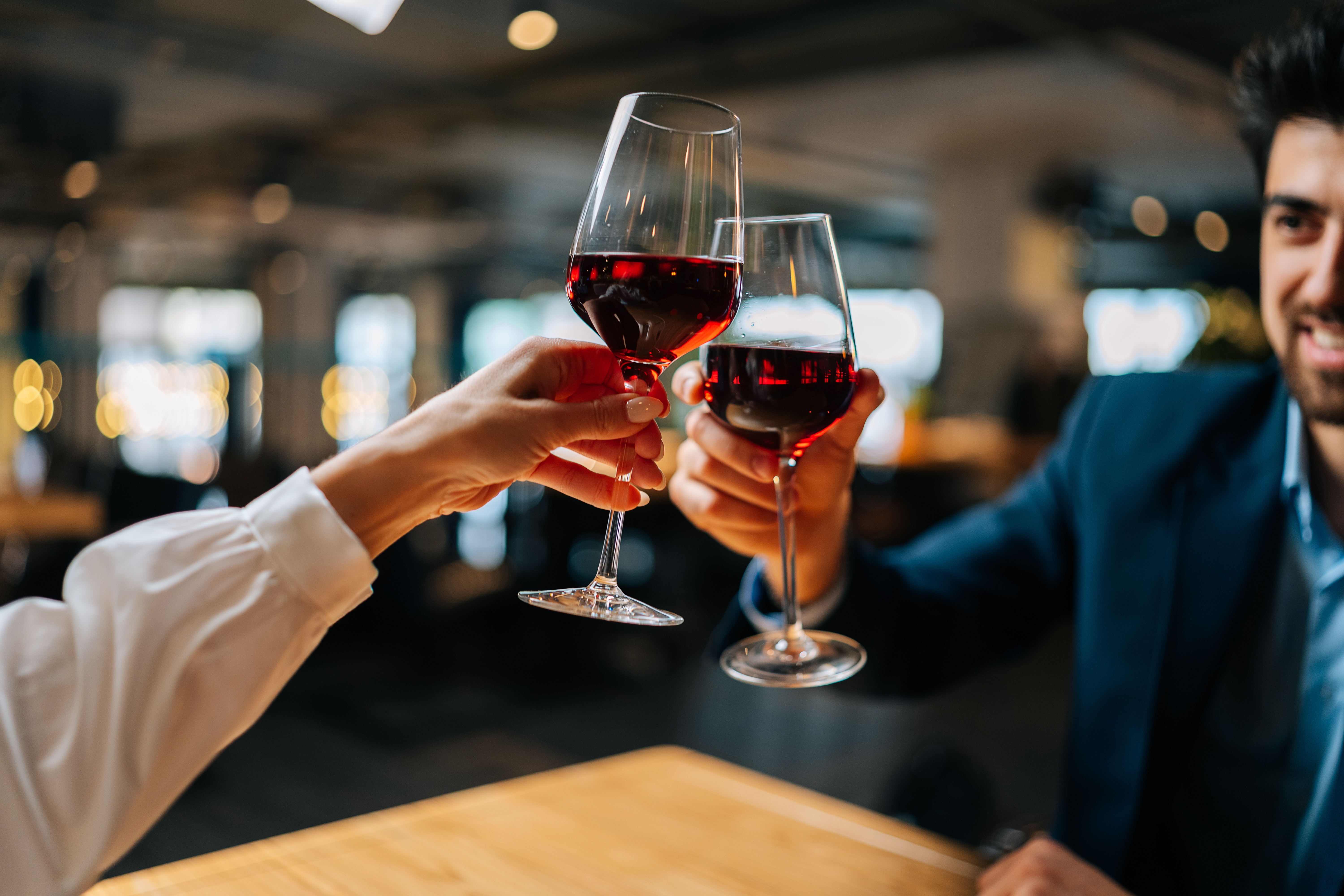 Two people toasting glasses of red wine in a restaurant