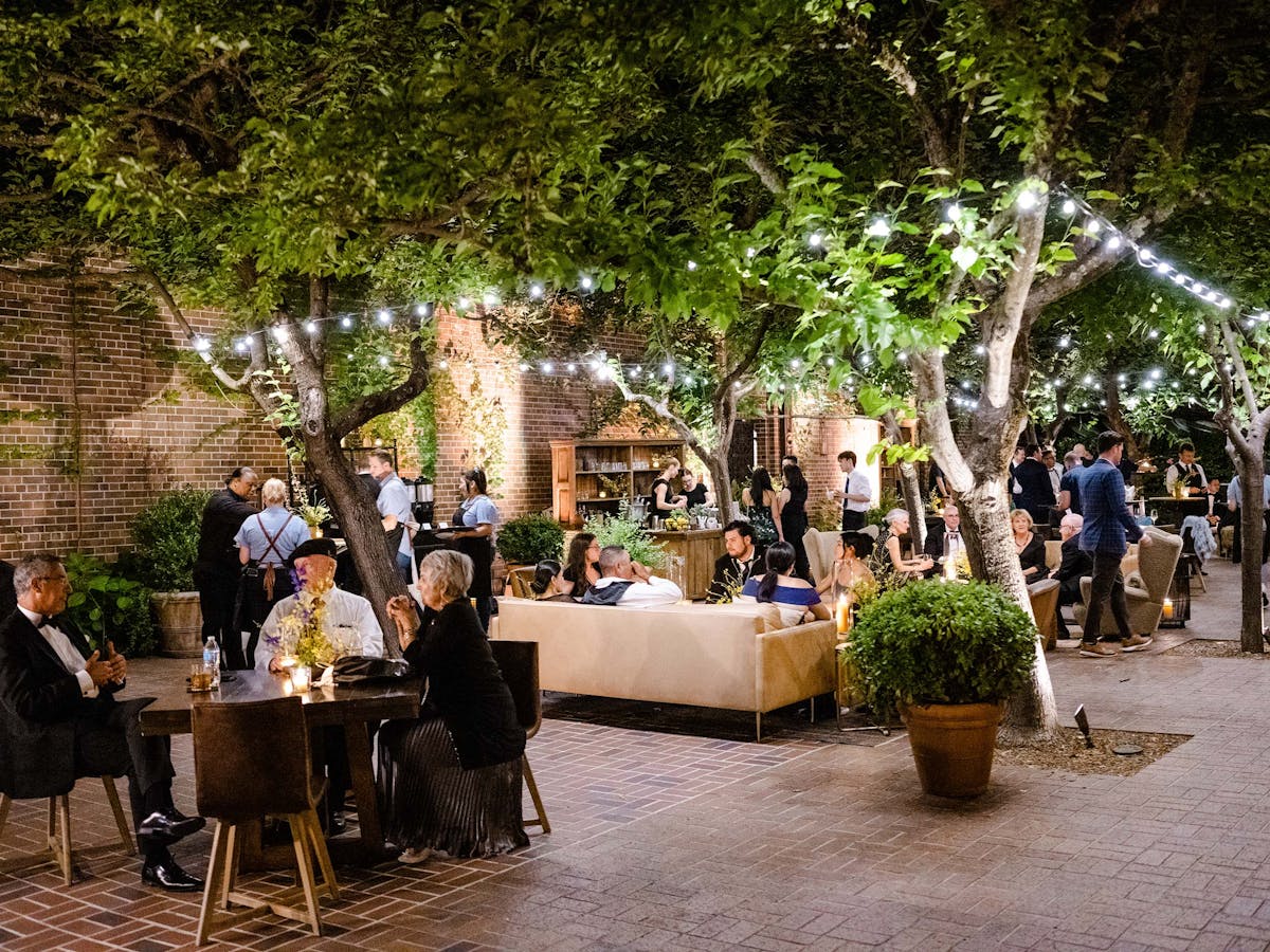 a group of guests dining on the charter oak patio with lights strung from the trees above