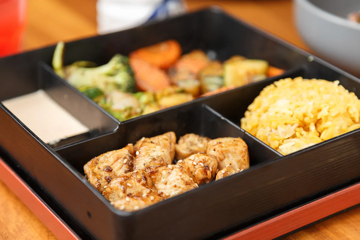 a tray of food filled with rice, meat, vegetables, and sauces