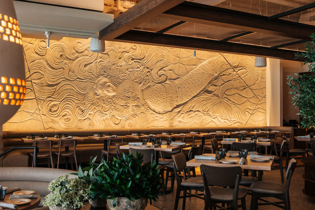 a room with tables and chairs and a wall with a mermaid sculpture