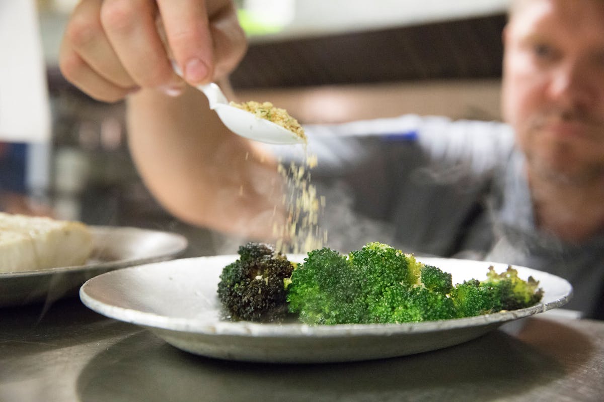 a person sitting at a table with a plate of food with broccoli