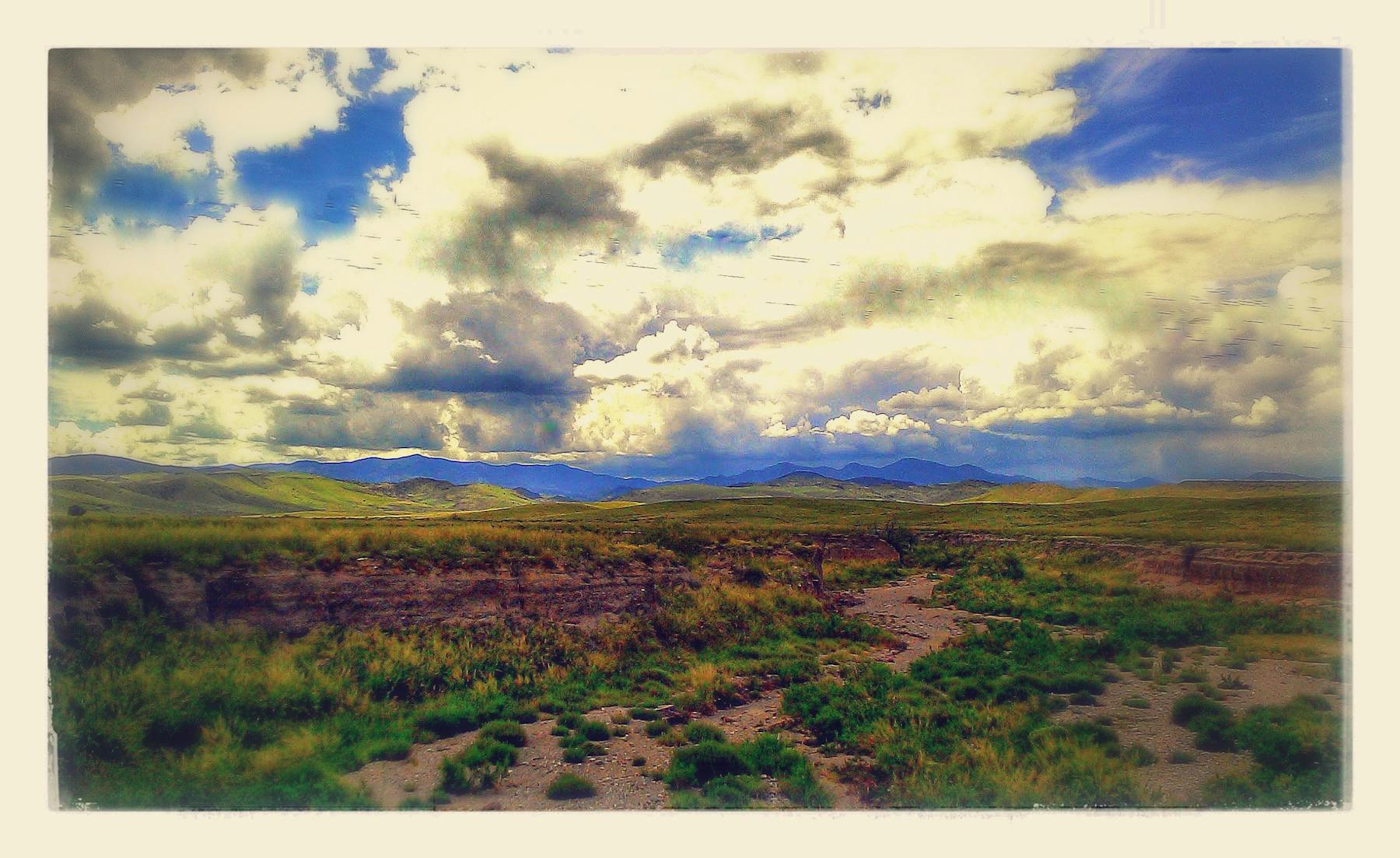 a large green field with clouds in the sky