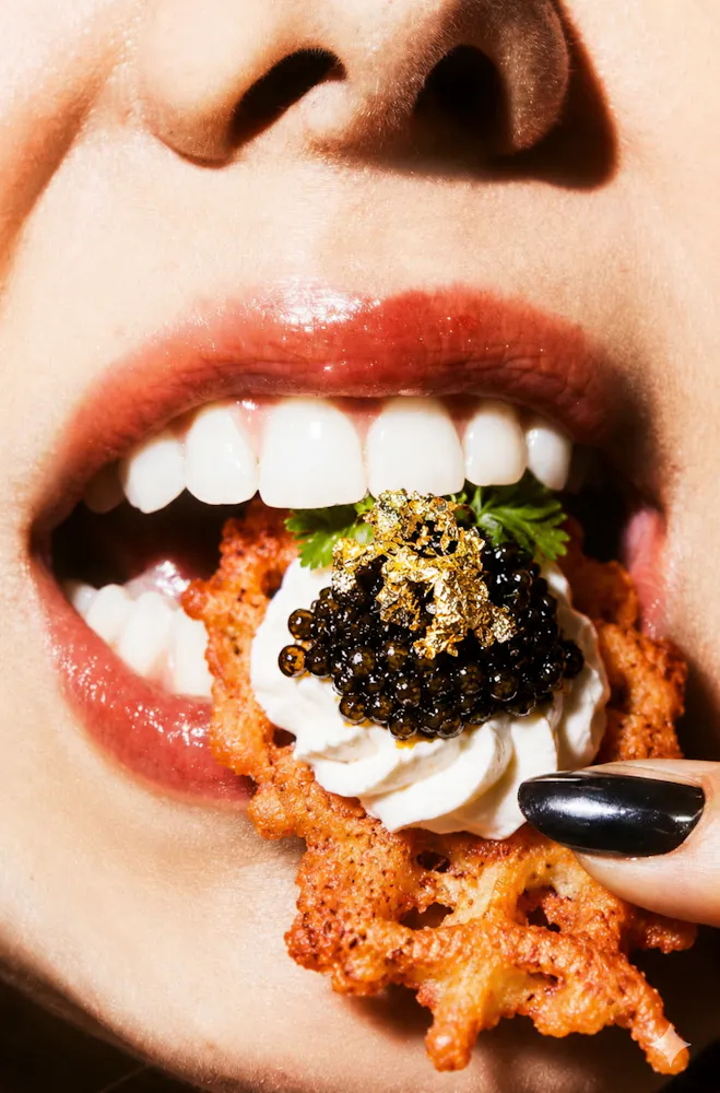 Potato Latkes topped with caviar and gold flakes going into a women's mouth at Caspians Rock & Roe