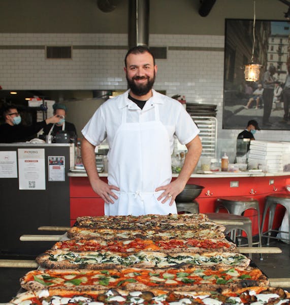 a man standing in front of a large pizza