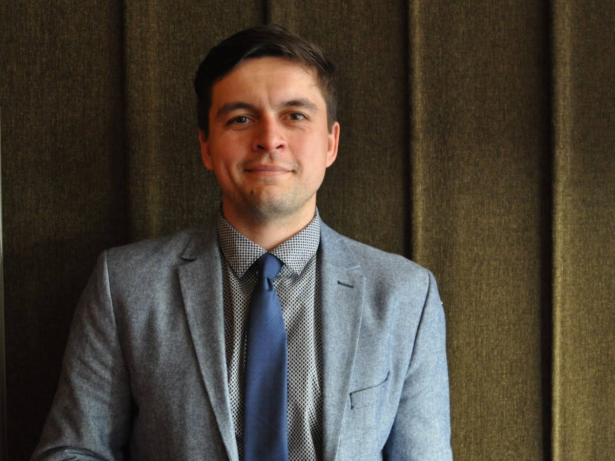 a man wearing a suit and tie smiling at the camera