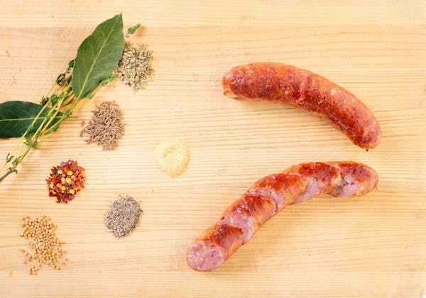 Smoked bratwurst on a cutting board next to herbs and spices.