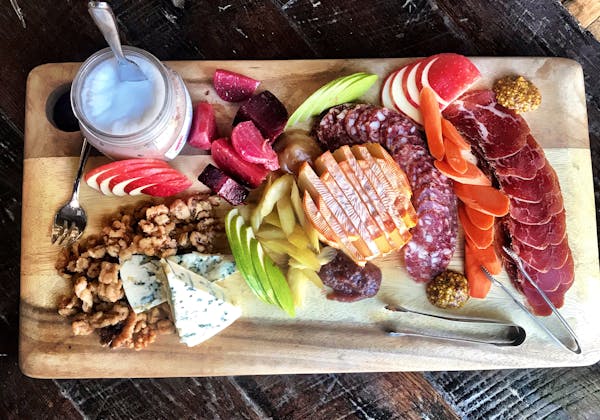A fall harvest inspired charcuterie board shot from above. The board contains different cheese, cured meats, season fruits and veggies, and candied walnuts.