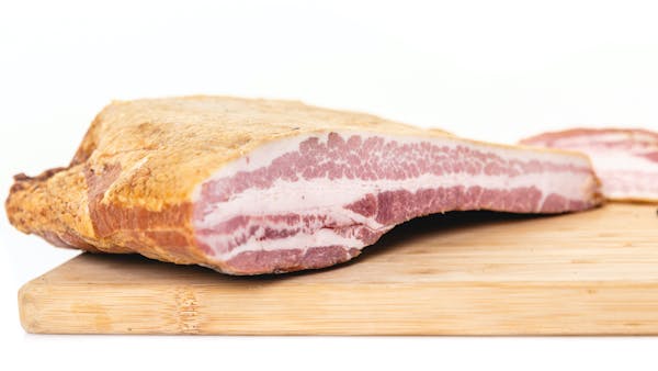 A whole chub of bacon shot from the side close up to show the marbled fat and muscle.