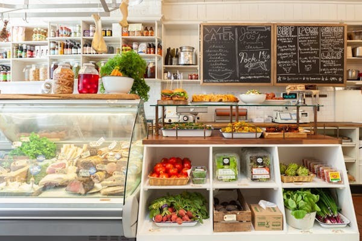the interior of a butcher and grocery shop displaying various cheeses and vegetables