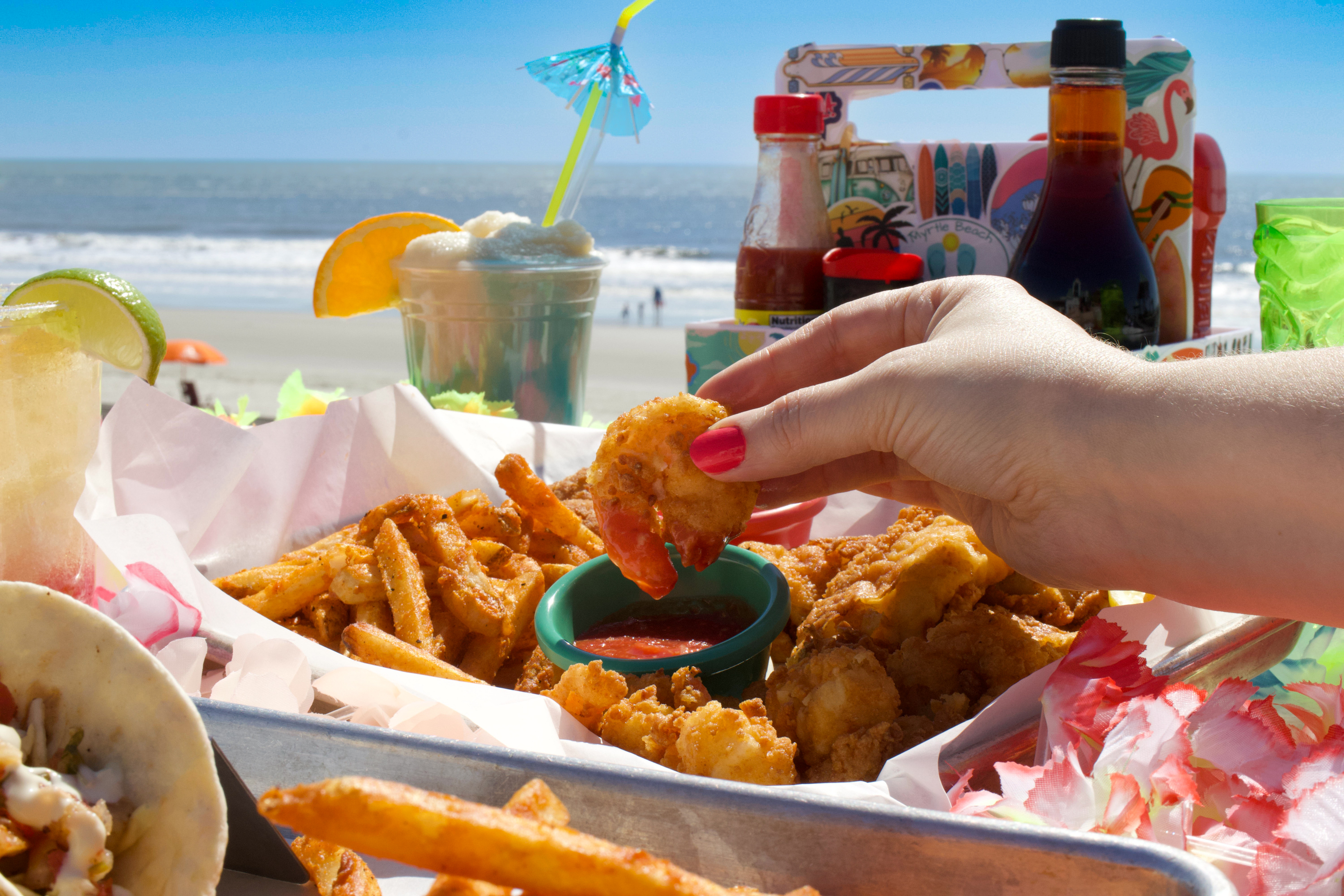 a hand dipping a shrimp into a bowl of french fries