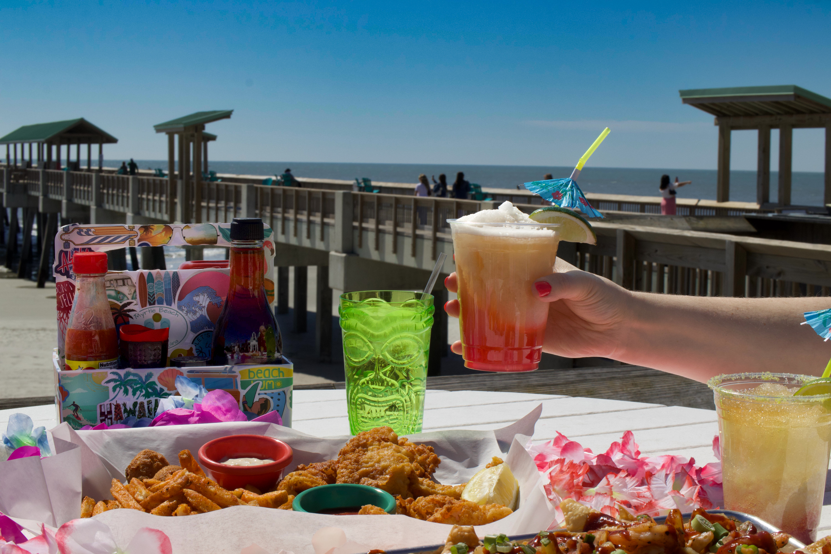 a hand holding a drink with a drink and a tray of food on a table