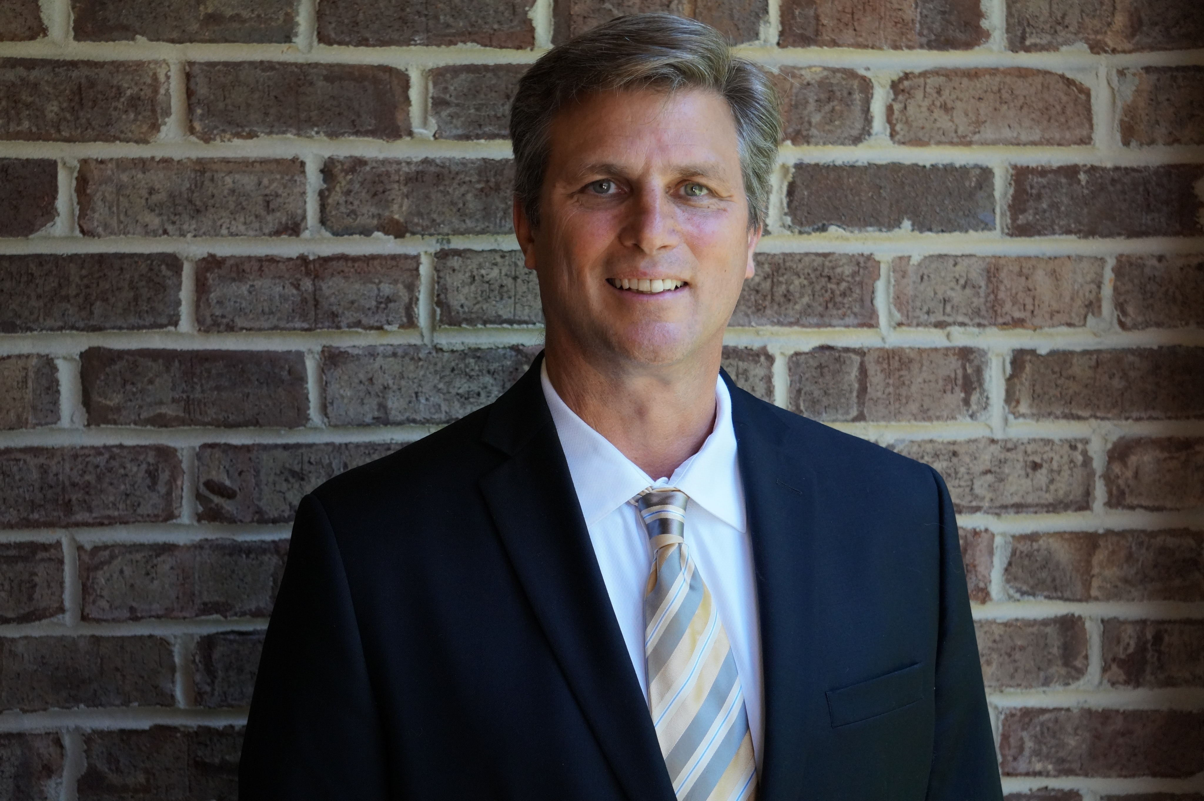 a man wearing a suit and tie standing in front of a brick wall