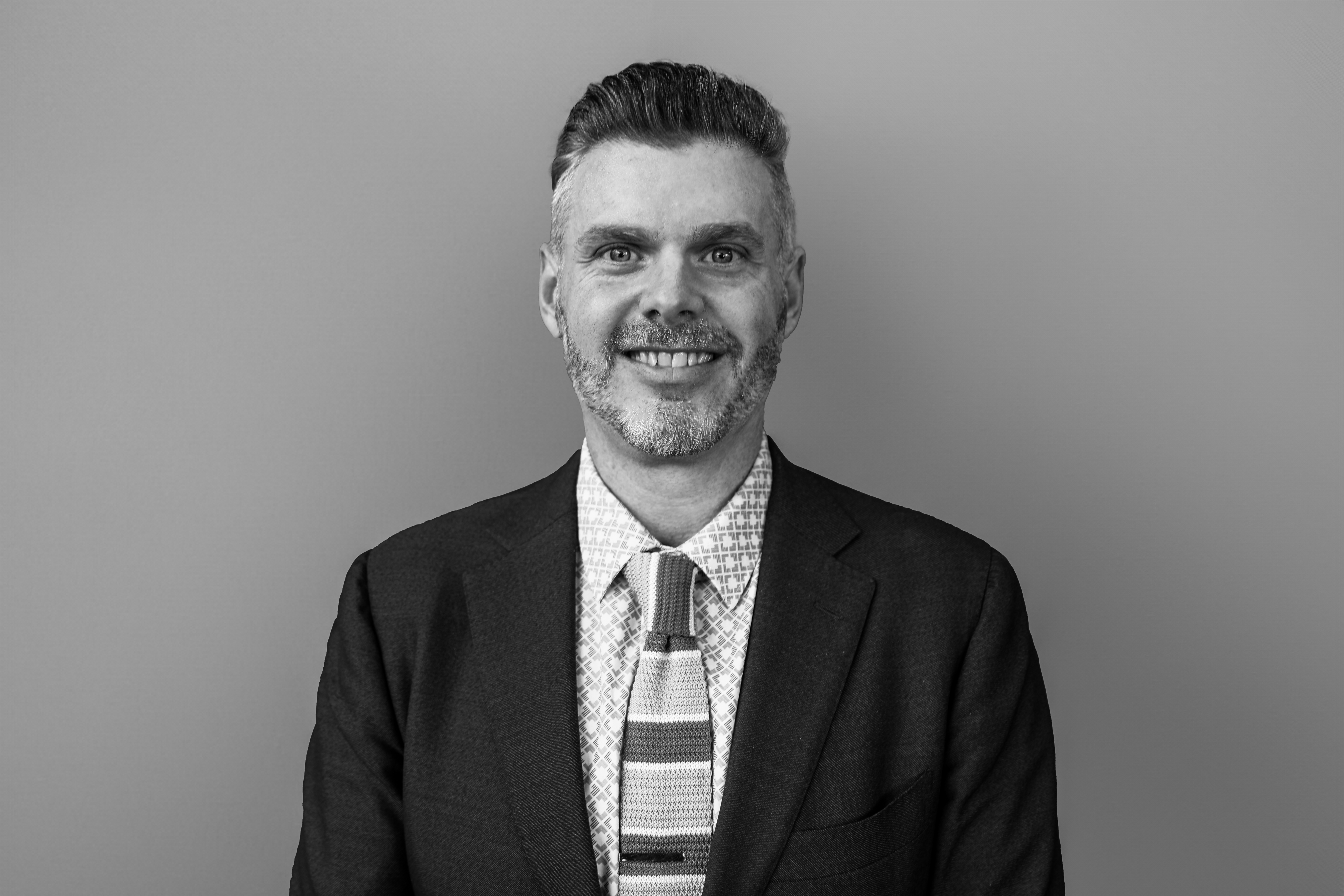 a man wearing a suit and tie smiling at the camera