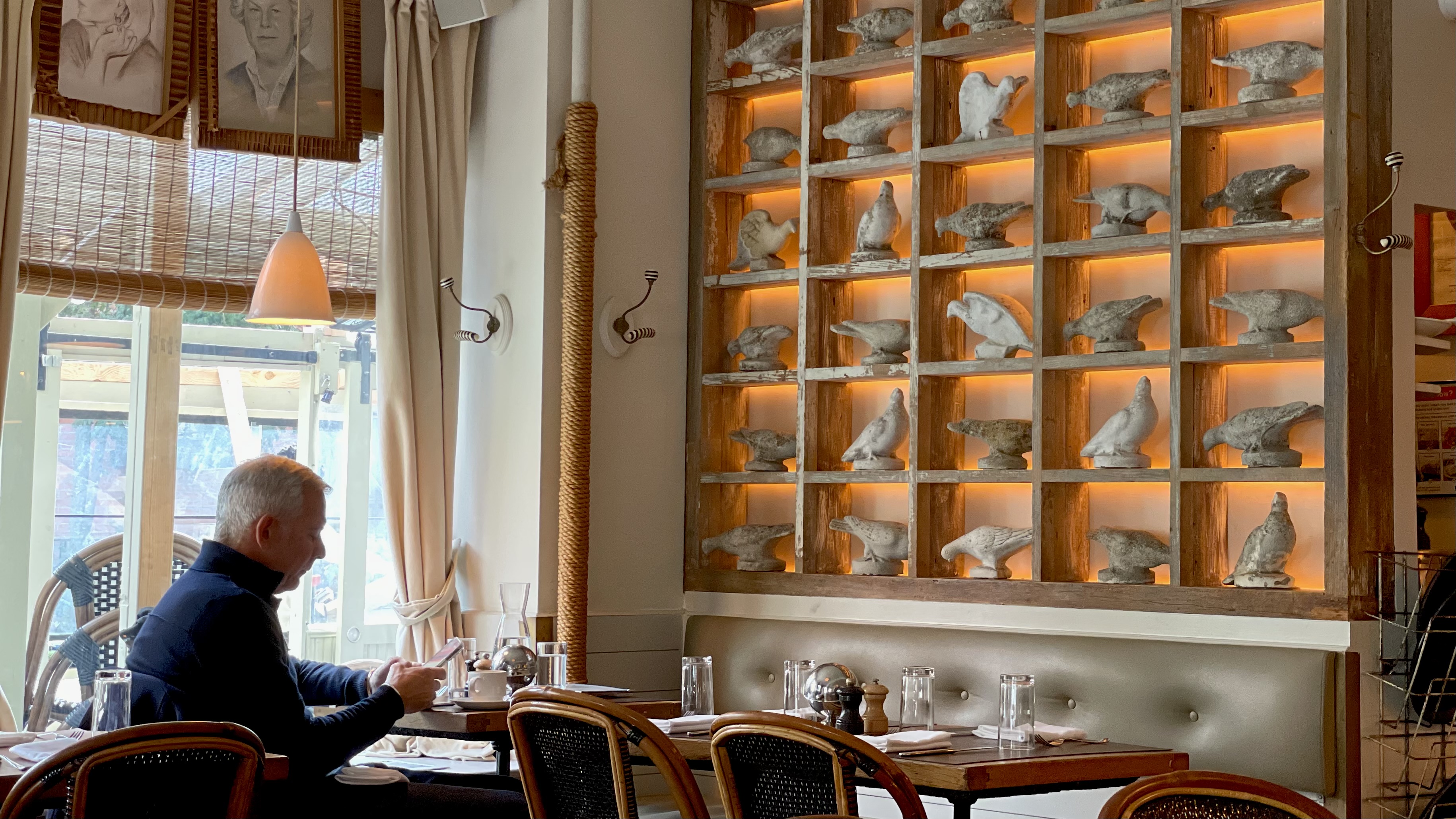 breakfast patron reading complimentary news papers over a hot cup of rich tasting coffee ordering breakfast in front of of a wall of iconic stone bird sculptures warmly backlit