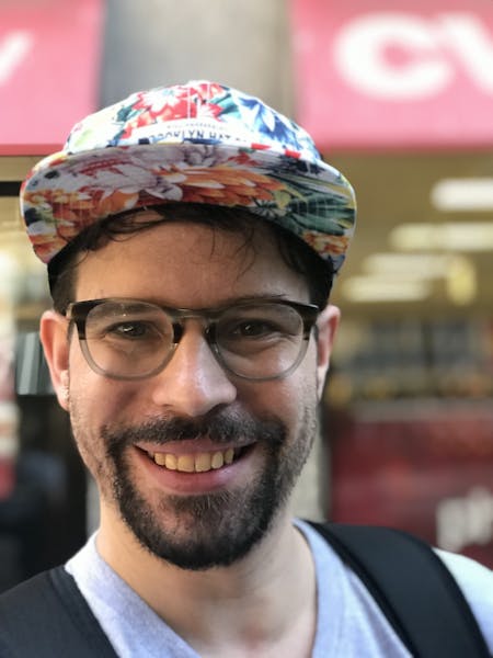 a man wearing a hat and glasses smiling for the camera
