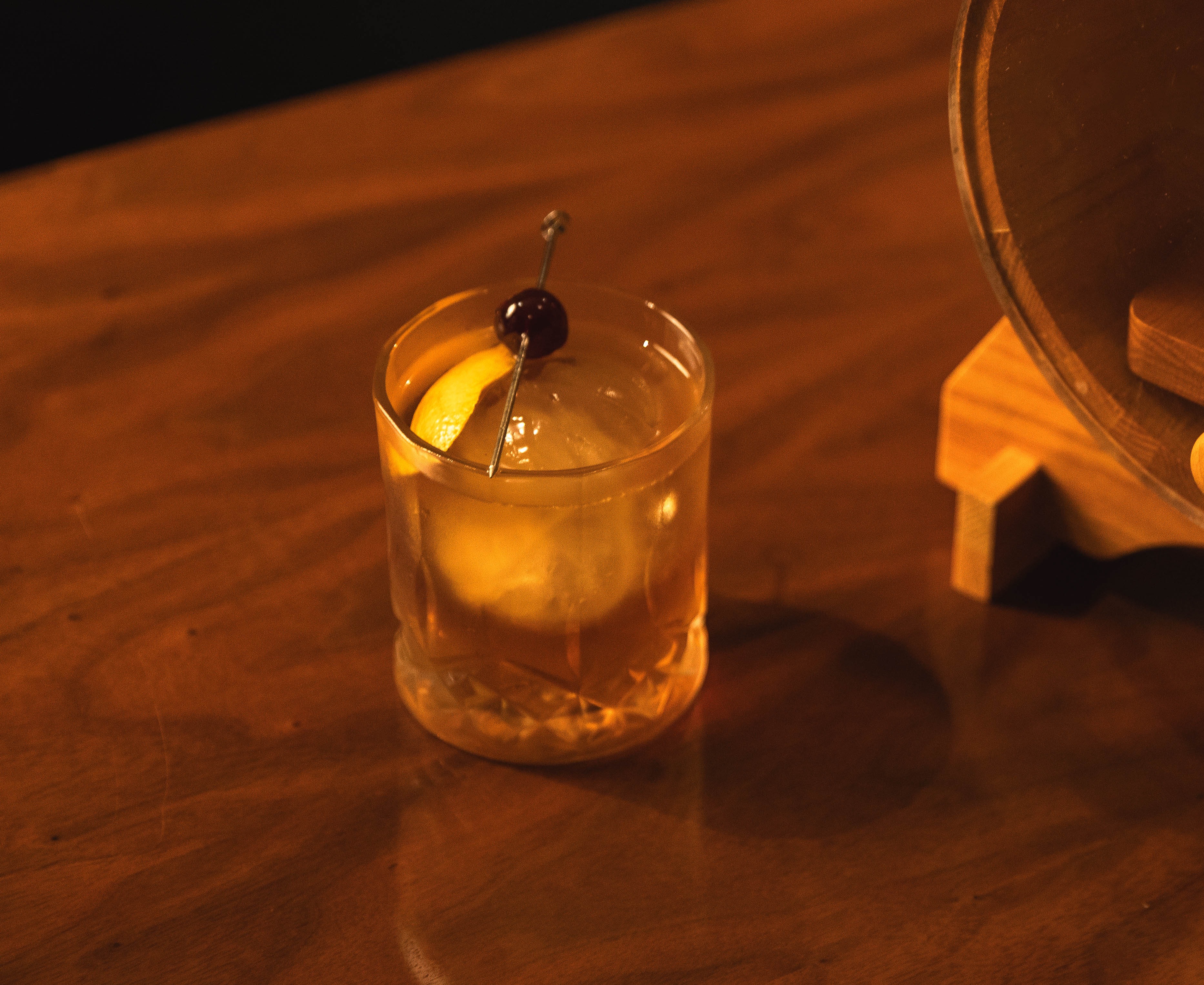 Old Fashioned–style cocktail with large clear ice sphere, an orange peel, and a cherry garnish