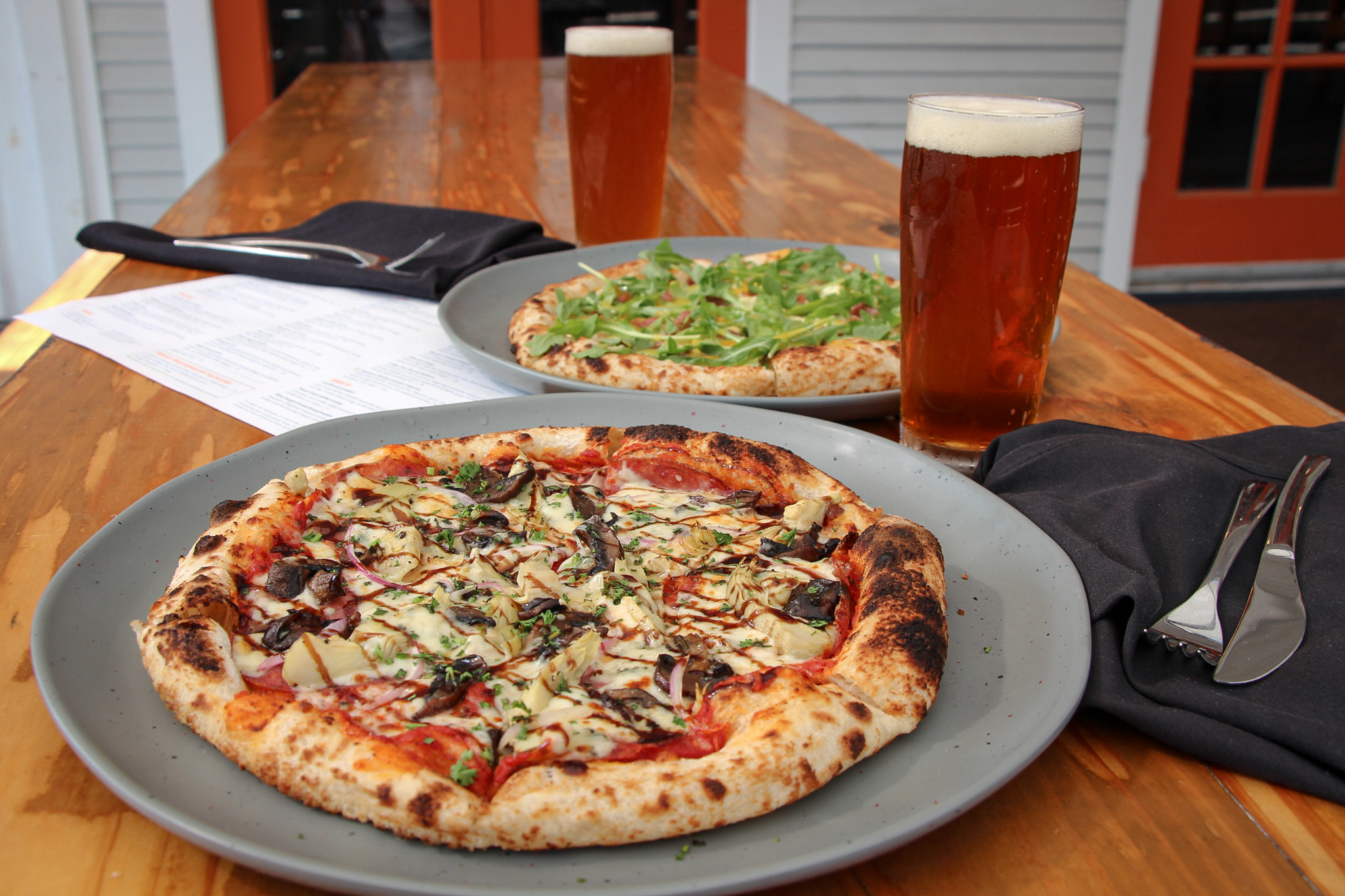 wood-fired pizza sitting on top of a wooden table with craft beer