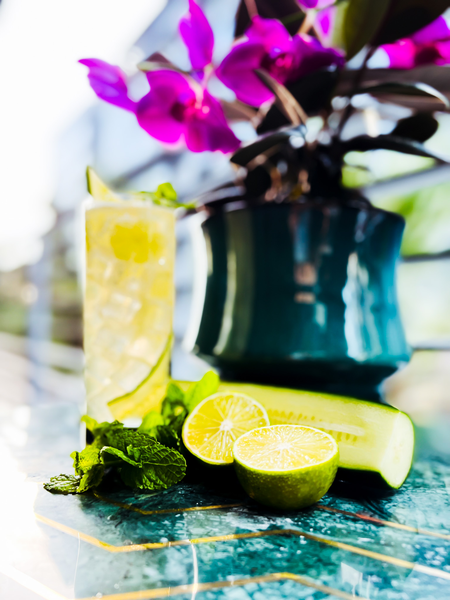 a vase filled with purple flowers on a table with a cucumber and gin cocktail