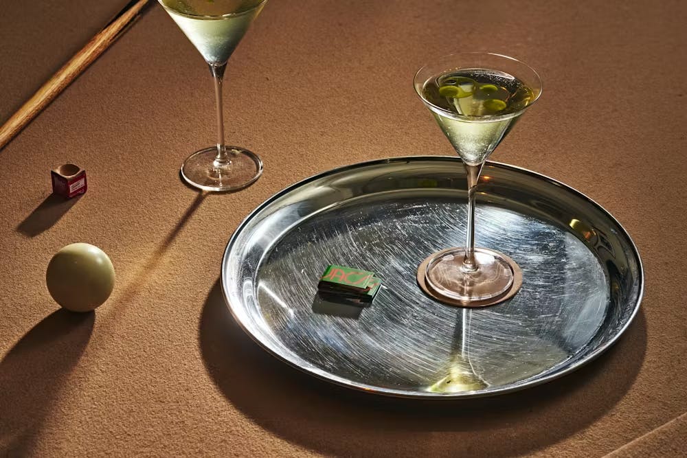 two Casino Royal martinis on a pool table with matchbooks and a tray