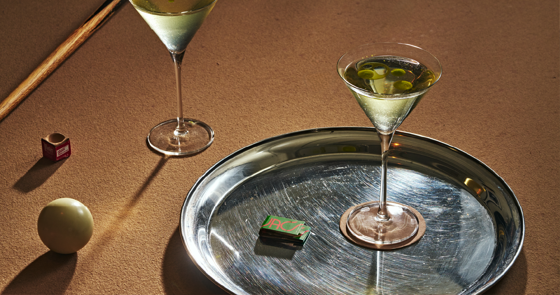 Two Martinis on a pool table with a silver tray and a branded Jac's matchbook