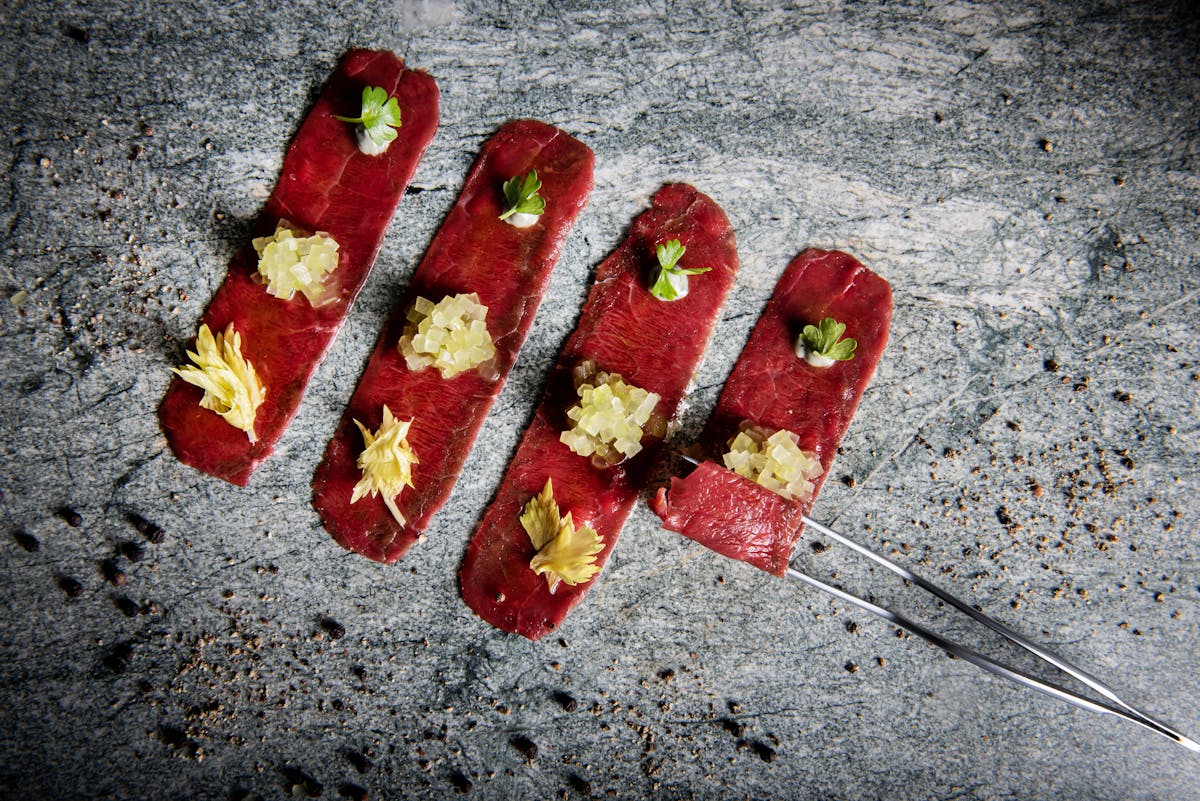 a tong rolling up thinly sliced meat.