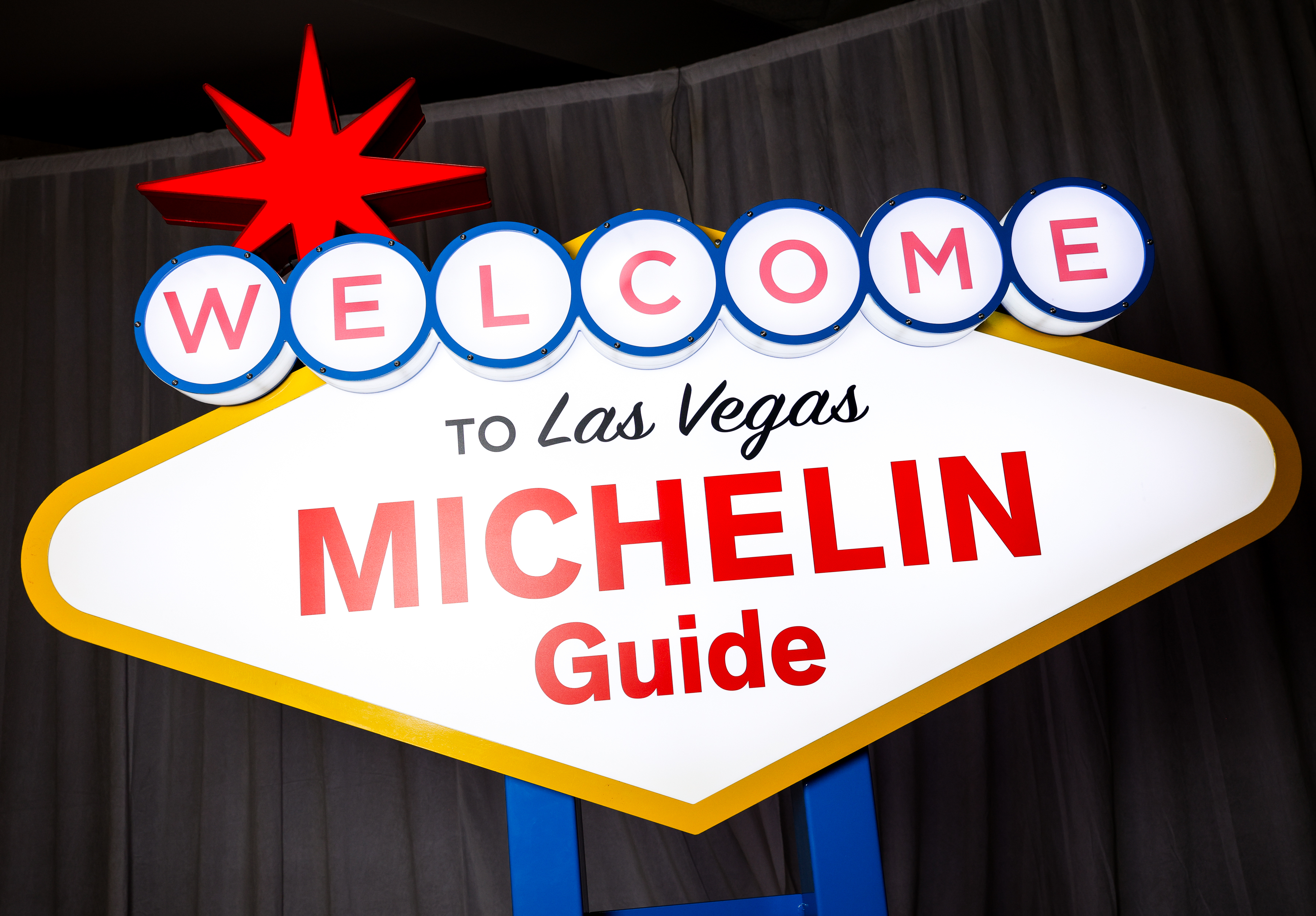 a sign with a red star and blue text with Welcome to Fabulous Las Vegas sign in the background