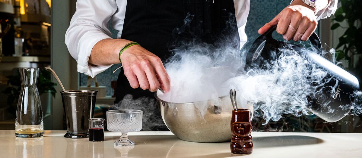 A man in a black apron is skillfully pouring a drink
