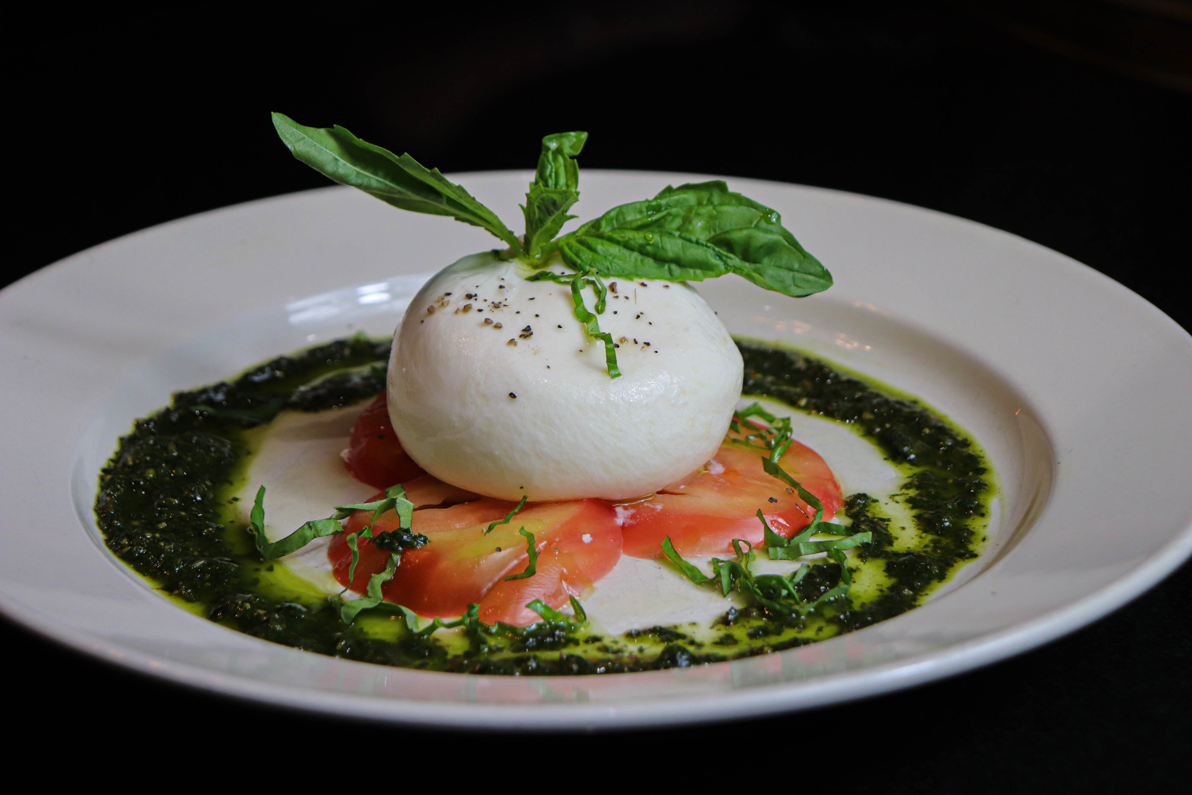 a plate of food with a white ball on top of tomatoes and basil