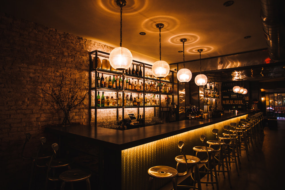 a long bar table in an upscale dark, moody room serving cocktails