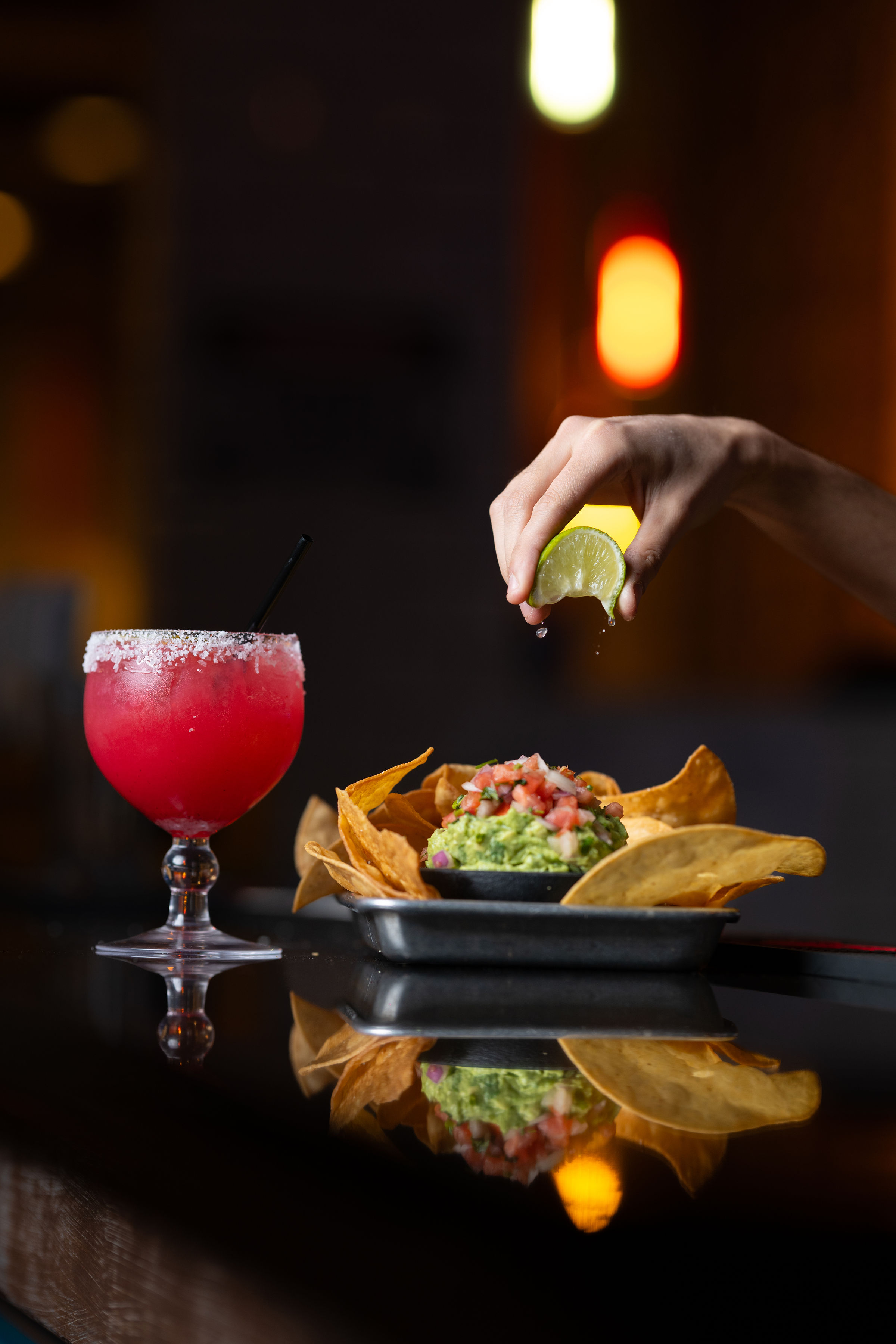 a hand squeezing lime over a bowl of guacamole and a drink