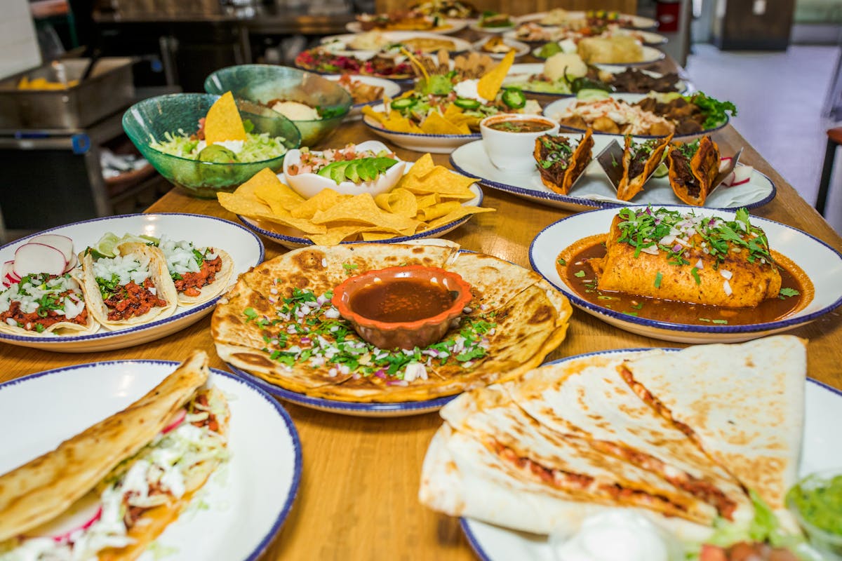 a table with many plates of mexican food, including quesadillas, tacos, etc. 