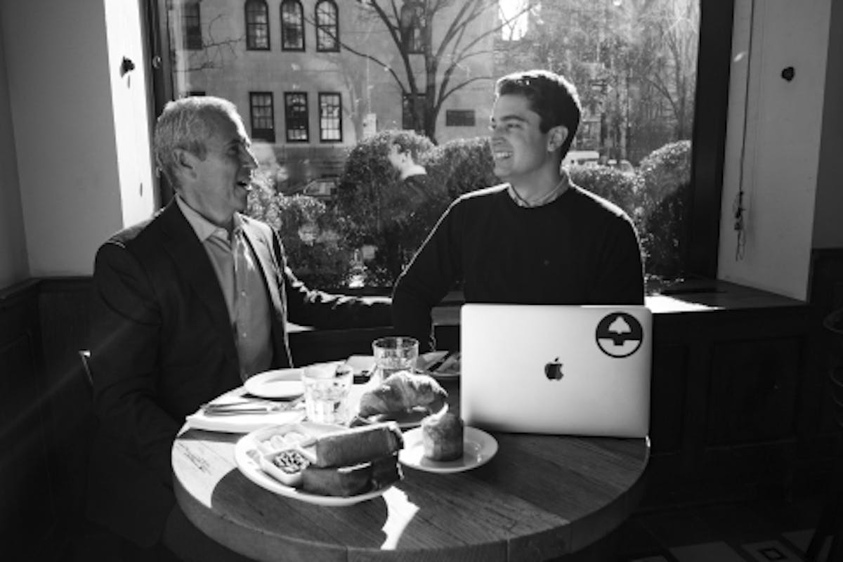 a person sitting at a table with a laptop and smiling at the camera